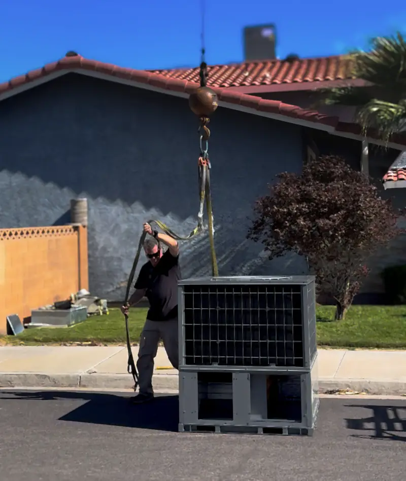 Manring technician guiding a new air conditioning unit as a crane lowers it in front of a Las Vegas home
