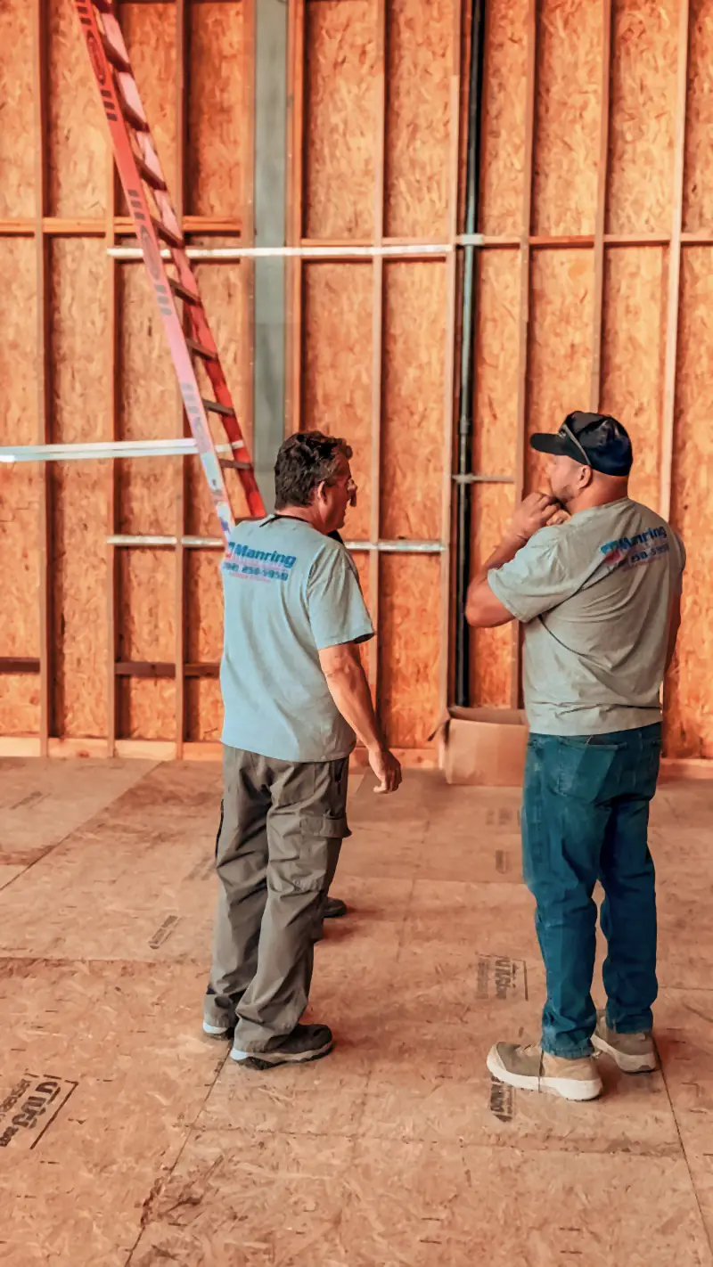Two Manring team members planning an HVAC install inside a framed new build