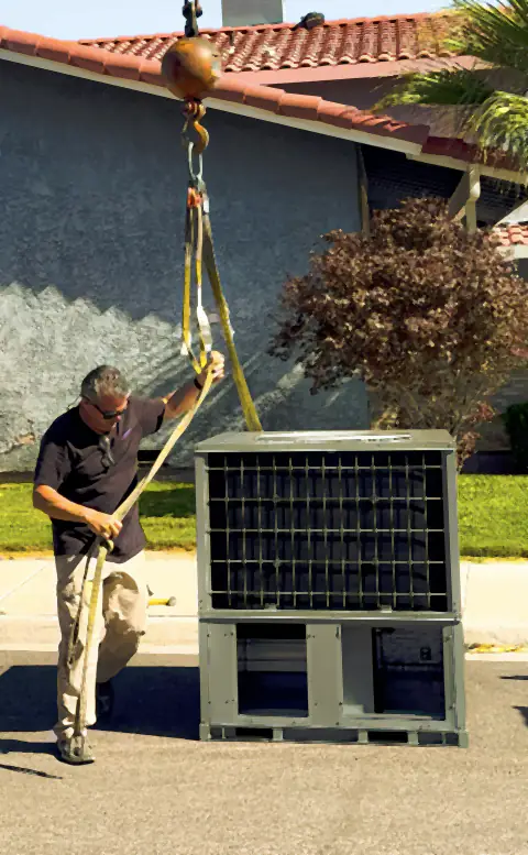 Adjusting the rigging as a large air conditioning unit is lifted by crane in front of a house